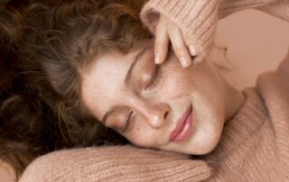 Woman with curly auburn hair and warm peachy skin tone wearing a blush sweater