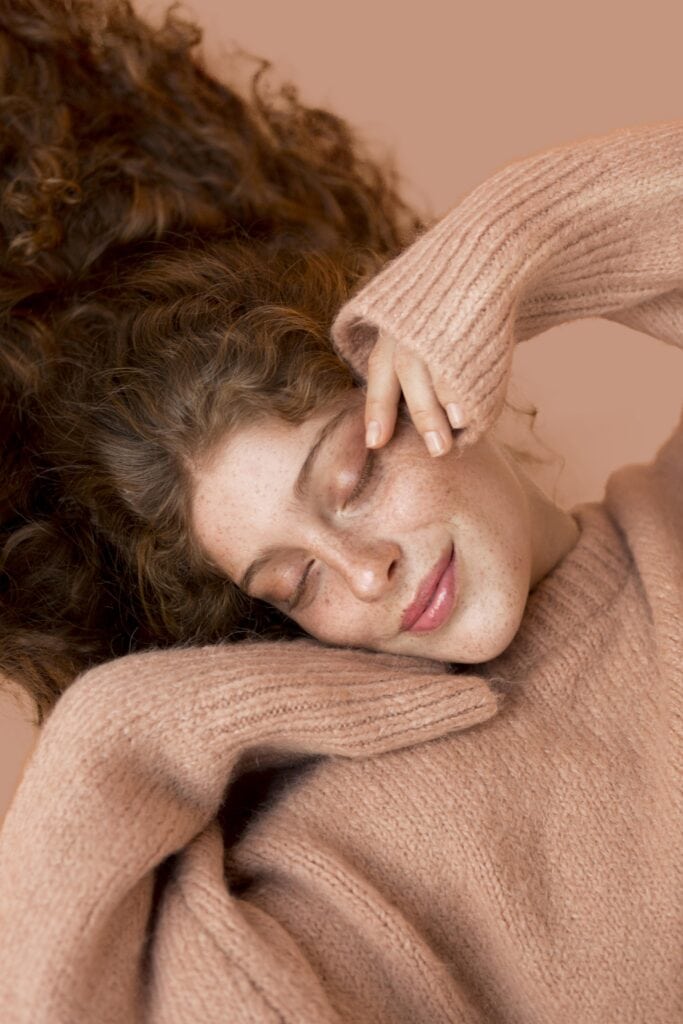 Woman with curly auburn hair and warm peachy skin tone wearing a blush sweater