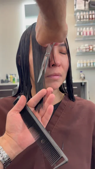 Stylist cutting a dark bob with scissors and comb